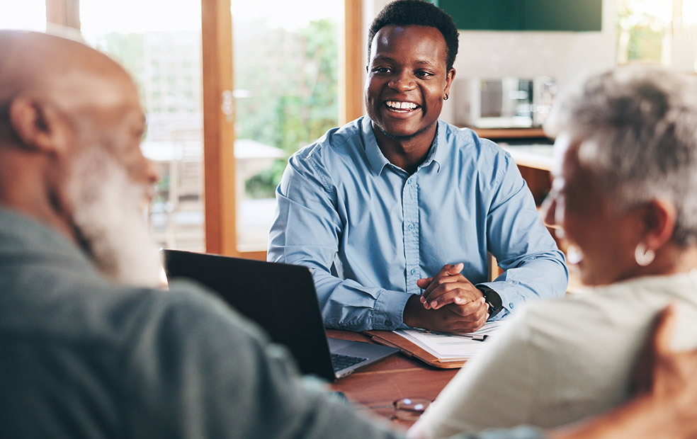 Financial advisor meeting with two clients at a table, reviewing documents and a laptop in a professional office setting