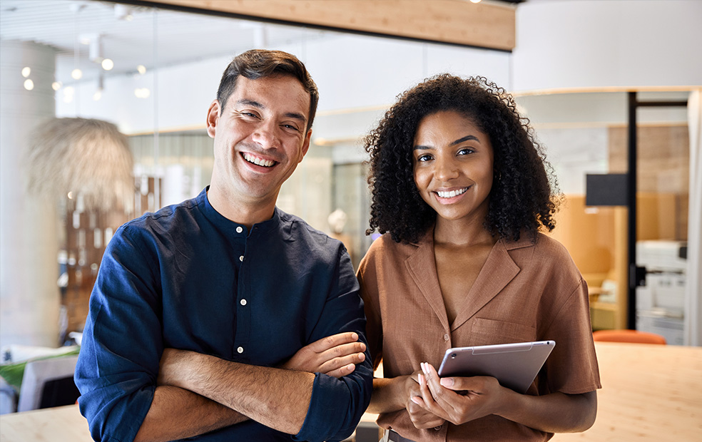 Two financial professionals standing together in a modern office, with one holding a tablet.
